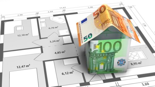 Aus Euro-Banknoten gefaltetes Haus auf einem Bauplan als Symbol für Wohneigentum, Immobilienfinanzierung und private Altersvorsorge.