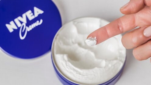 Geöffnete Dose Nivea Creme mit entnommener Hautcreme auf einer Fingerspitze.