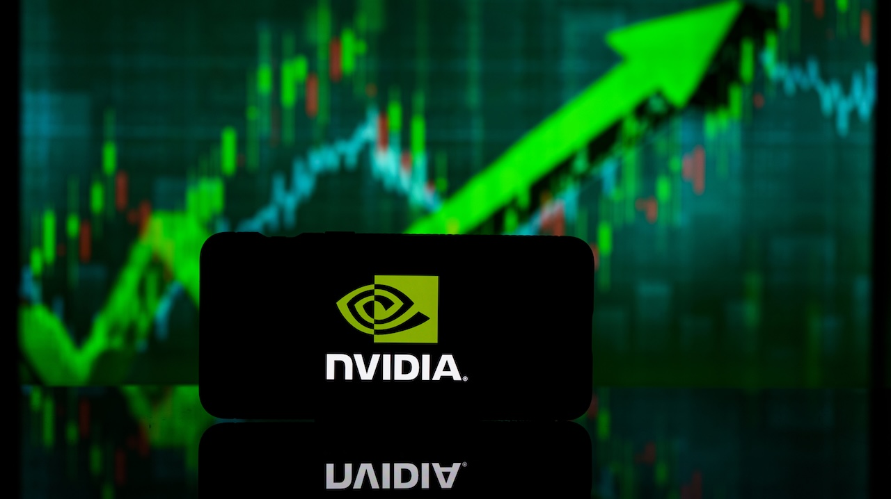 Smartphone mit NVIDIA-Logo auf dem Display vor einem etwas verschwommenen grünen Aktienkurs, der nach oben zeigt.