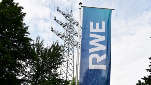 RWE-Fahne vor einem Strommast und Hochspannungsleitungen.
