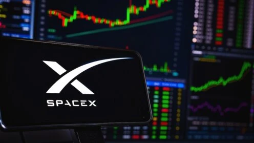 Smartphone mit SpaceX-Logo vor mehreren Börsenbildschirmen mit Kurscharts und Handelsdaten als Symbol für die Reaktion der Finanzmärkte auf die Unternehmenszahlen.