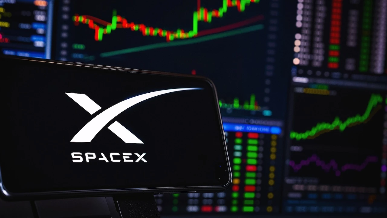 Smartphone mit SpaceX-Logo vor mehreren Börsenbildschirmen mit Kurscharts und Handelsdaten als Symbol für die Reaktion der Finanzmärkte auf die Unternehmenszahlen.