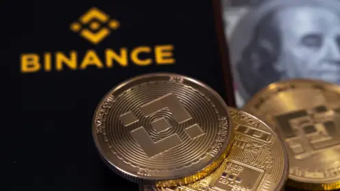 Binance-Logo auf schwarzem Hintergrund neben mehreren Kryptowährungs-Münzen mit Binance- und Bitcoin-Symbol, im Hintergrund unscharf ein Geldschein.