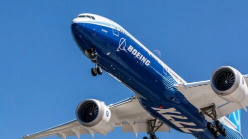 Eine Boeing-Passagiermaschine mit Boeing-Schriftzug ist von schräg unten vor tiefblauem Himmel im Gegenlicht zu sehen.
