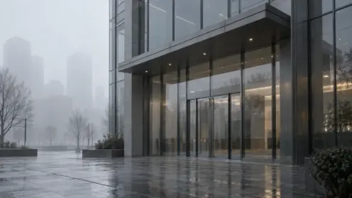 Verschlossene moderne Bürofassade im Morgennebel ohne Menschen, grauer Himmel spiegelt sich im Glas.