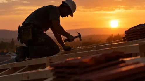 Dachdecker arbeitet im Gegenlicht auf einem frischen Dachstuhl bei Sonnenuntergang.