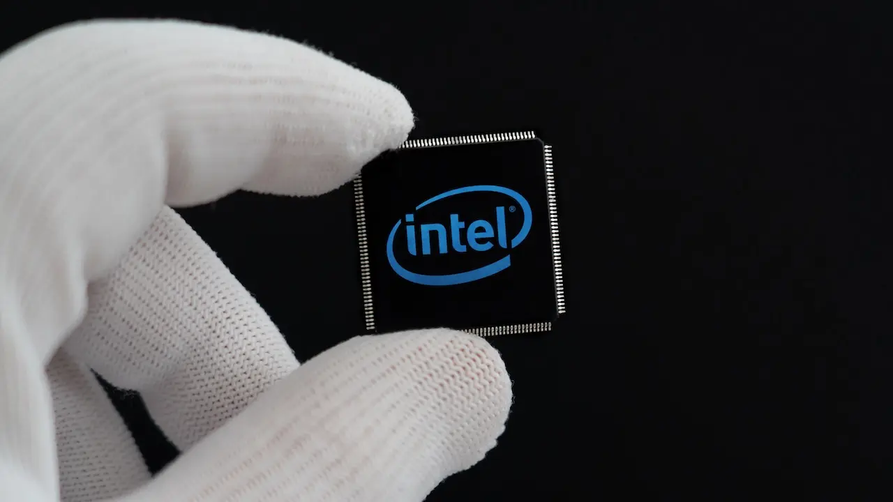 Eine behandschuhte Hand hält einen kleinen schwarzen Mikrochip mit dem blauen Intel-Logo vor schwarzem Hintergrund.
